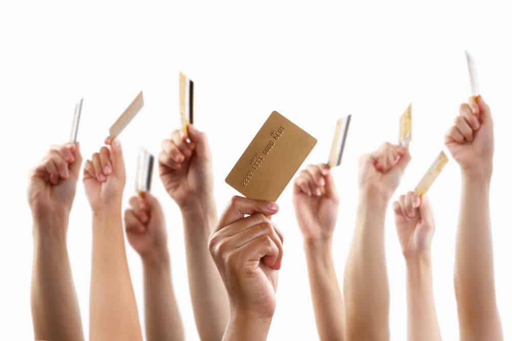 Lot of hands raising and holding gold credit card, against white background