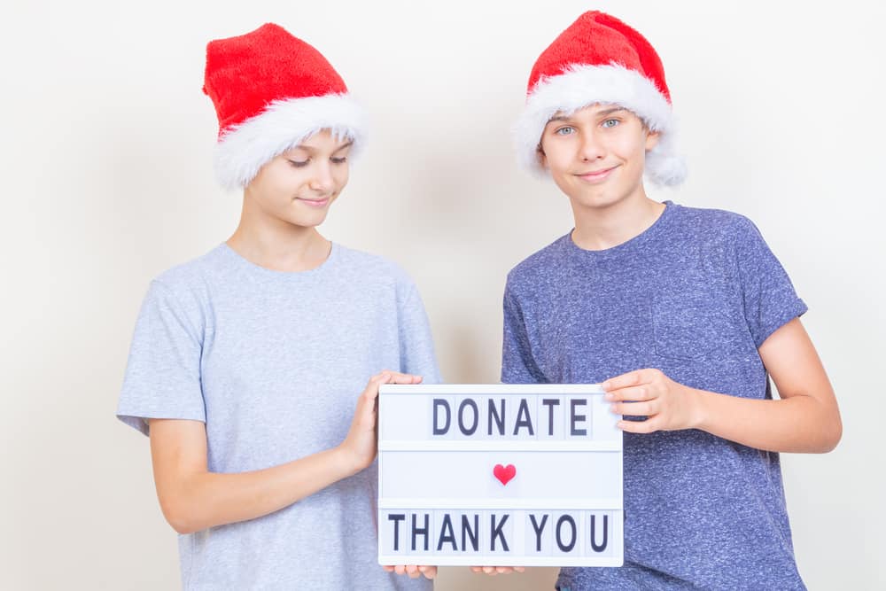 Christmas donation, charity. Teenager boys volunteers with red Santa hat holding lightbox with message Donate and Thank you.